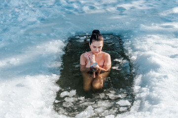Girl with bikini and a watch in frozen lake ice hole. Woman hardening the body in cold water. Good...