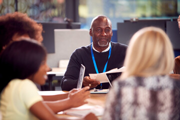 University Or College Students Sitting Around Table With Tutor Collaborating In Seminar On Laptop