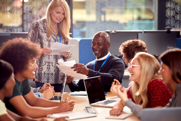University Or College Students Sitting Around Table With Tutor Collaborating In Seminar On Laptop