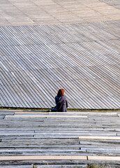 Woman sittin on the wooden stairs of an amphitheater in vertical
