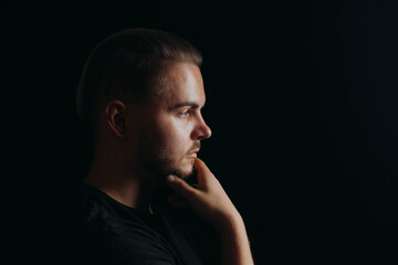 Fototapeta na wymiar Portrait of caucasian attractive guy with beard and hair on black background. Man holds hand to chin and looks and meditation about prospects. Serious person is focused on thoughts and opinion