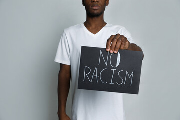 African American man holding sign with phrase No Racism on grey background, closeup