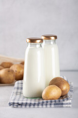Vegan plant based milk in two bottles. Alternative potato milk and potato tubers on gray table