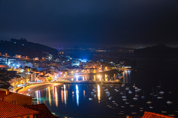 Pueblo costero de noche  en la ría de Pontevedra con playa y barcos en el puerto iluminado