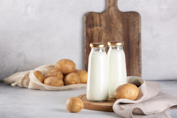 Vegan plant based milk in two bottles. Alternative potato milk and potato tubers on gray table