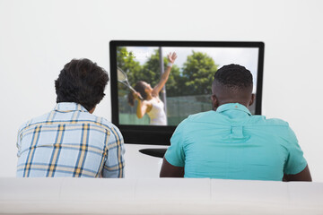 Fototapeta premium Rear view of two friends sitting at home together watching tennis on tv