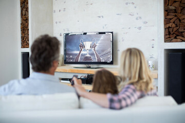 Rear view of family sitting at home together watching sport event on tv
