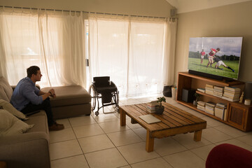 Caucasian disabled man sitting at home watching sport event on tv