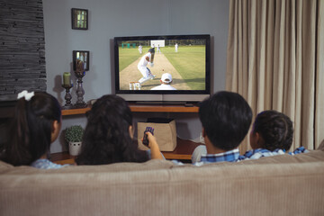 Rear view of family sitting at home together watching cricket match on tv
