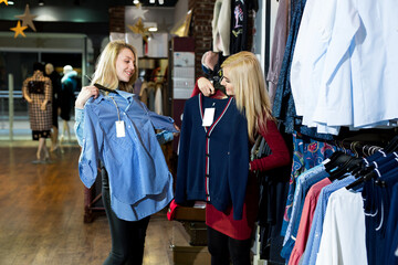 Fototapeta premium Two happy female best friends looking at the quality of a shirt hanging on a rail inside the clothing store