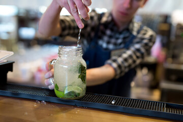 The bartender crushes ice for a Mojito cocktail on the bar