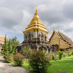 Fototapeta premium Scenic view of Chedi Chang Lom stupa with vihara in background at historic Lanna style Wat Chiang Man buddhist temple, the oldest in Chiang Mai, Thailand