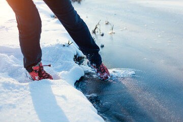 Dangerous thin ice. Woman takes risk to step on frozen river surface in winter. Caution, unsafe...