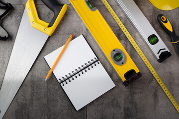 Contractor theme. Tool kit of the contractor: yellow hardhat, libella, hand saw. Plans and notebook on the gray tiles background. © zolnierek