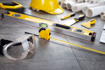Contractor theme. Tool kit of the contractor: yellow hardhat, libella, hand saw. Plans and notebook on the gray tiles background. © zolnierek