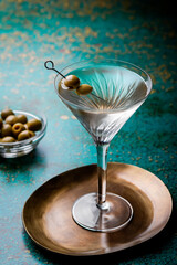 Dirty martini cocktail in martini glass with olives garnish on green colored table