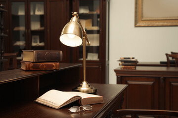 Books, glasses and lamp on wooden table in library reading room