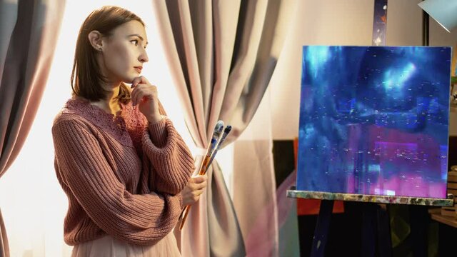 Nft painting. Crypto art. Non-fungible token. Pensive female artist viewing abstract blue pink glitch noise animation digital artwork on canvas in home studio interior.