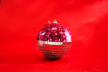Christmas holiday background. Unusual combination of usual things. Disco ball as an fruit pomegranate against a red background. Copyspace. 