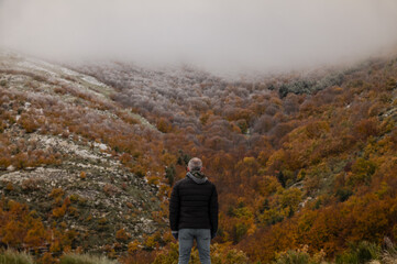 Naklejka na ściany i meble Portrait of adult man in black winter jacket against autumn color trees on mountain, in Tejera Negra, Cantalojas, Guadalajara, Spain