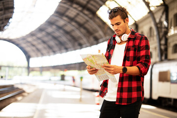 Happy young man waiting for the train. Beautiful smiling man with city map in subway...