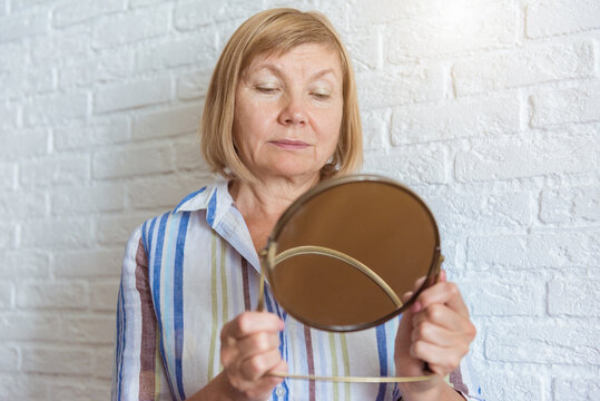 Sad Old Senior Mature Woman Looking At Face Reflection In Round Mirror. Domestic Life, Home Spa, Self Care And Pampering Concept