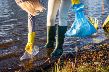 Volunteer picking up plastic bottle from polluted lake or river. Environmental damage. Water...