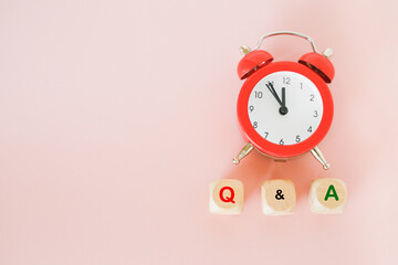 Q and A text on wooden blocks and red analog alarm clock on sweet pink background with copy space