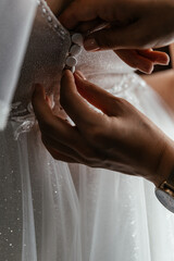 Bride being helped to fasten corset on white wedding dress