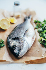 close-up of raw dorado fish on parchment against a background of parsley and sliced ​​lemon on a white background