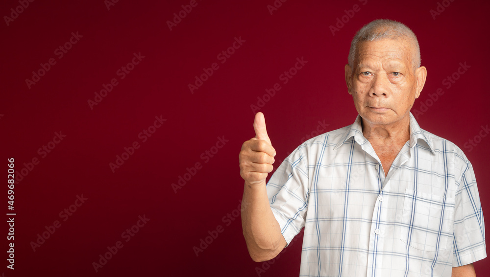 Poster portrait of a senior man showing thumbs up and looking at the camera with a smile while standing ove