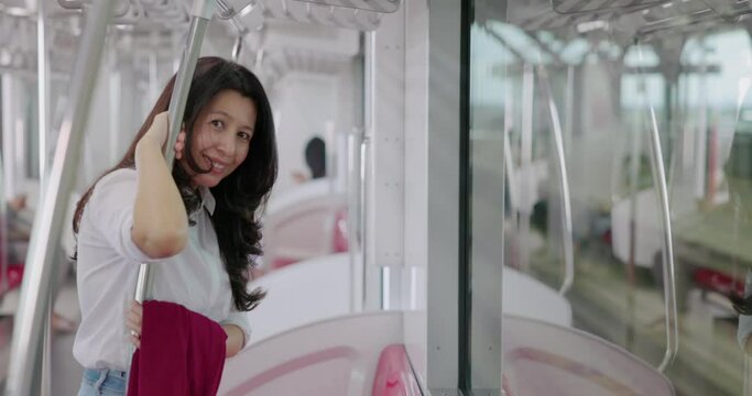Asian woman relaxing enjoying view during morning and looking at camera while standing Sky train or High speed train. Asian businesswoman looking out the window in travel transport.