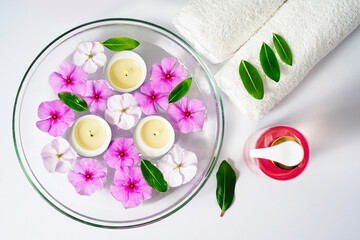 Body care supplies, white towel, oil and rose flowers on a white background, Burning floating candles in a bowl of water, spa relaxation and meditation