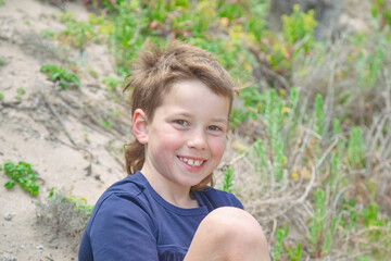 Aussie boy with mullet sitting on sand dune at the beach