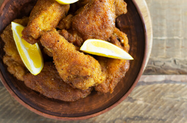 Crispy chicken wings and legs, breaded with lemon wedges in a ceramic plate on a wooden background. Junk food concept. Top view.