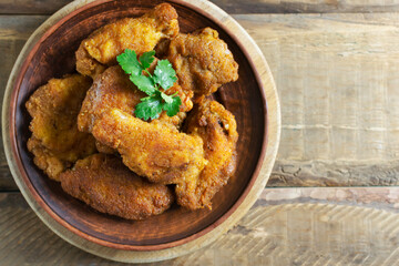 Crispy chicken wings and legs, breaded with cilantro leaves in a ceramic plate on a wooden background. Japanese Christmas food. Top view. Copy spase.