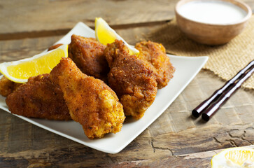 Breaded crispy chicken wings and legs with lemon slices, sauce and bamboo sticks on a wooden background. Japanese Christmas food. A traditional dish.