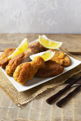 Breaded crispy chicken wings and legs with lemon slices, sauce and bamboo sticks on a wooden background. Japanese Christmas food. A traditional dish. Vertical orientation.