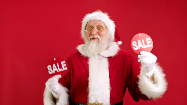 Christmas SALE. Cheerful Santa Claus is Dancing and Joyful From Christmas Sale Holding Two Banners With Inscription SALE Showing Off Inscriptions to Camera on Red Background.