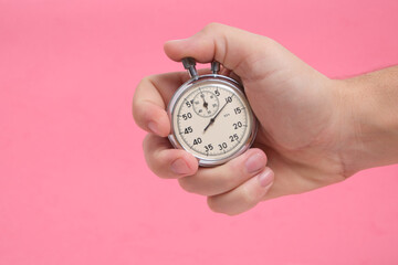 Man hand holding stopwatch on pink background.