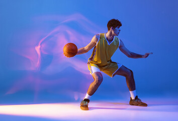 Fototapeta na wymiar Dynamic portrait of professional basketball player training with ball isolated on blue studio background in mixed neon light.