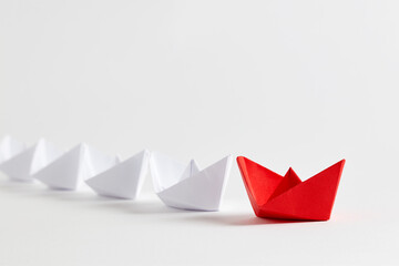 Red paper boat leads white paper ships. Teamwork, cooperation, leadership, partnership and participation