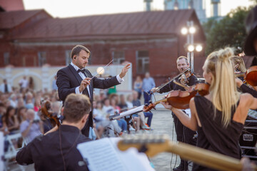 Conductor directing orchestra performance on the street - obrazy, fototapety, plakaty