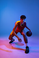 Fototapeta na wymiar Studio shot of young man, professional basketball player playing basketball isolated on blue background in neon light.