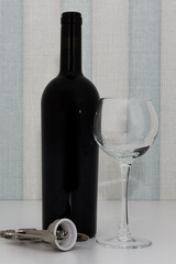 a bottle of red wine, a glass and a corkscrew on the table