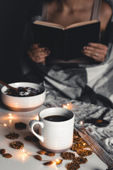 The woman is wrapped in a blanket and holds a book in her hands. cup of coffee . Christmas mood. 