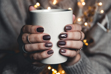 A woman in warm clothes of neutral tones with a Christmas garland. matte stylish manicure. gel...
