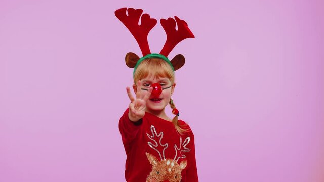 Countdown to holiday celebration. Cheerful toddler girl kid in Santa Christmas hat counting in reverse order from five to one on violet studio background. Win scream, winner gesture. Happy New Year