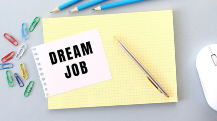 DREAM JOB is written on a piece of paper that lies on a notebook next to office supplies.