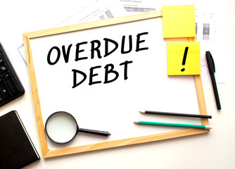 OVERDUE DEBT text is written on a white office board. Work table with office supplies.